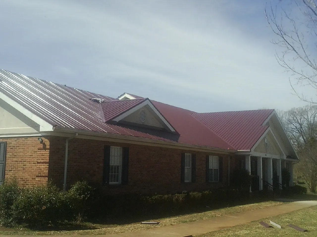 Red metal roof with gabled entries on a long brick building, from a Hail Damage Roof Repair job in Schiller Park