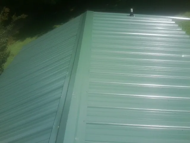 New green metal panels meeting at the ridge of a roof — Flat Roof Repair work by our crew in Schiller Park
