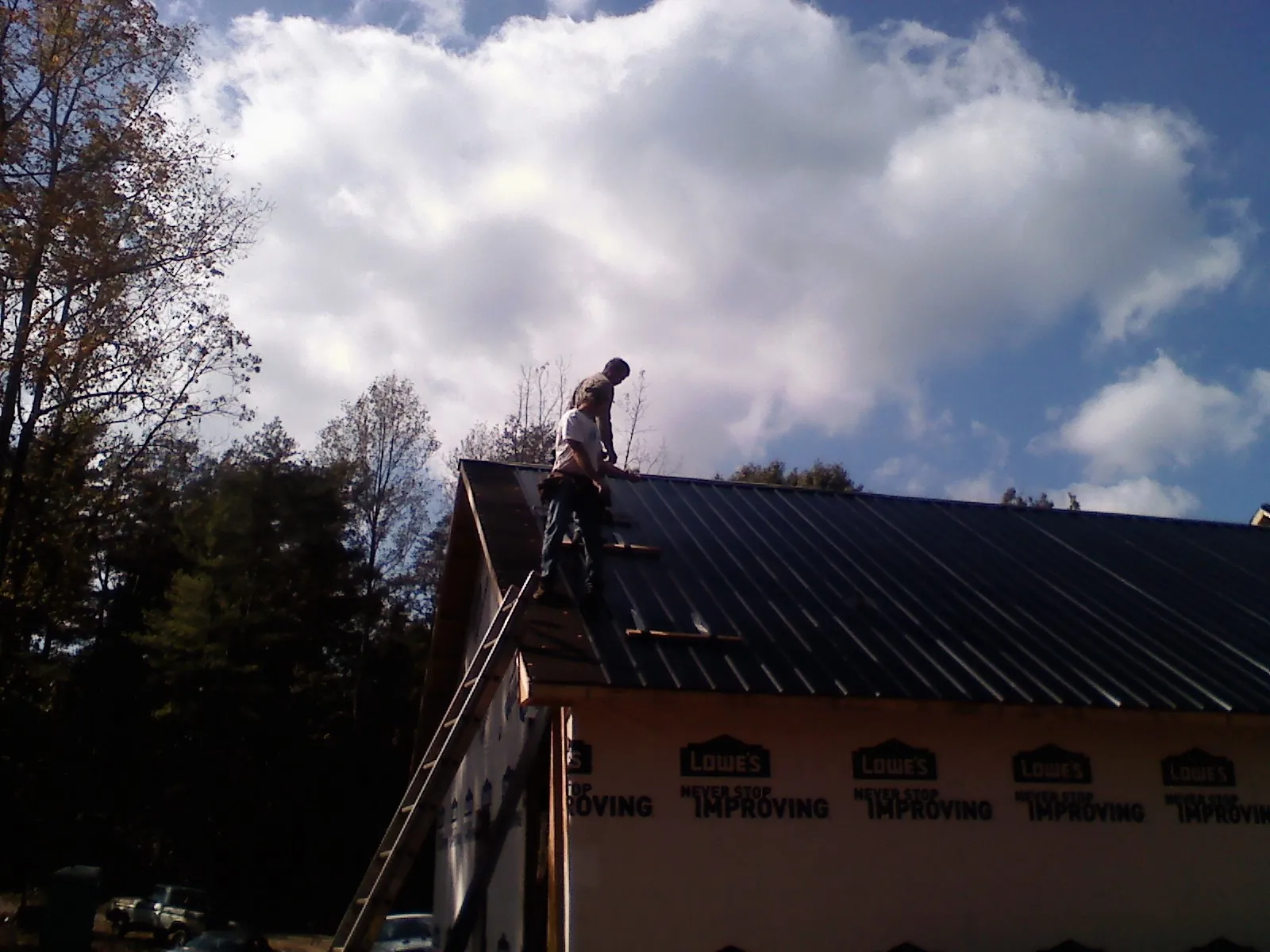 Roofer fastening dark metal panels high against a cloudy sky, from a Roof Inspection job in Schiller Park