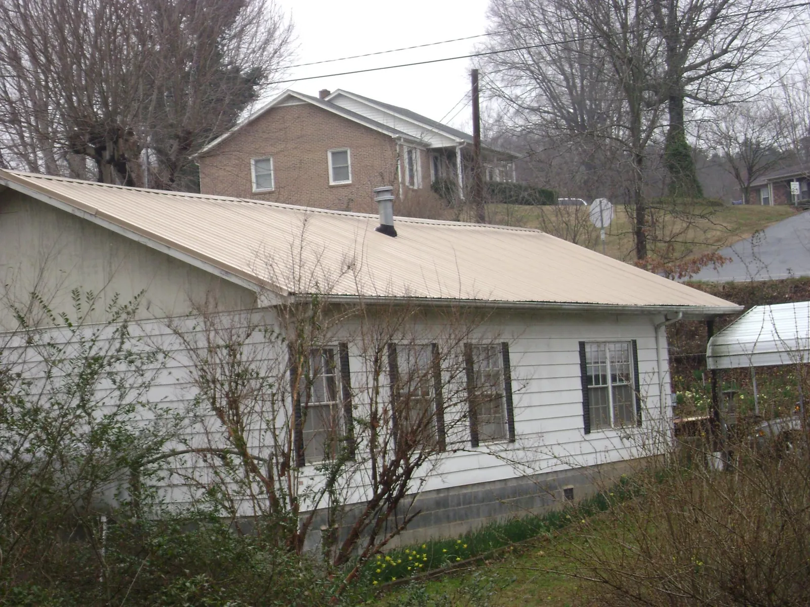 Tan metal roof on a white sided house set into a hillside — Commercial Roofing by Roofing Brothers in Schiller Park
